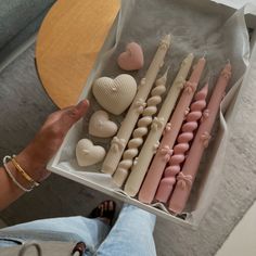 a person holding a box filled with candles and heart shaped candies on top of a table