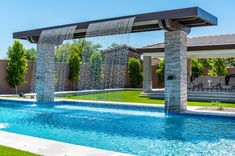 an outdoor swimming pool with waterfall and seating area in the background, surrounded by grass