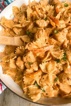 a white plate topped with pasta and meat next to a wooden spoon on top of a table