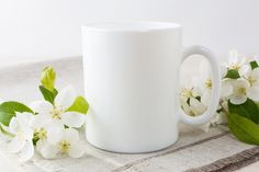 a white coffee mug sitting on top of a table next to some leaves and flowers