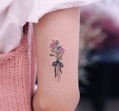 a woman's arm with a tattoo on it that has flowers and a bow