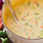 a bowl of broccoli cheese soup next to some carrots and other vegetables