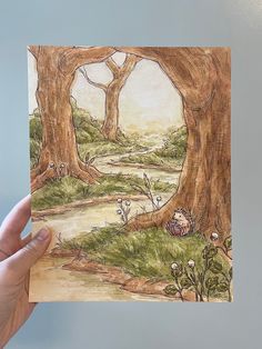 a hand holding up a drawing of a forest scene with trees and flowers in the foreground