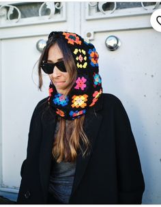 a woman wearing sunglasses and a knitted flower hoodie is standing in front of a white door