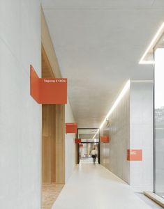 an empty hallway with orange and white signs on the walls, along with two people walking down one side