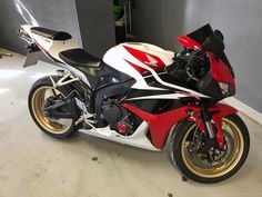 a red, white and black motorcycle is parked in a garage with no one around