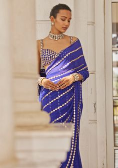 Introducing the showstopper saree set in royal blue hues. This exquisite set features a blue georgette saree adorned with delicate linear mirror hand embroidery, exuding timeless beauty. Teamed with a stunning modern cut blouse embellished with real hand-cut mirrors, it adds a touch of glamour to the outfit. Embrace elegance and make a statement with the blue linear saree, perfect for Mehendi, sangeet ceremonies, or as a wedding guest. Composition : Saree & Blouse - Georgette Care: Dry Clean Only and Vacuum Storage This product can be customized for sleeves, length and colour Delivery : 6-8 weeks as the product is hand crafted. Check Size Guide or choose MySize for free customisation (All Sizes above XL can be made at 15% additional cost) For more information and sizes please contact fabil Blue Georgette Saree, Mirror Blouse, Vani Vats, Cut Blouse, Vacuum Storage, Indian Wedding Wear, Georgette Saree, Georgette Sarees, Wedding Wear