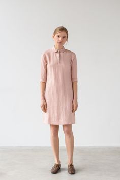 "An A-cut dress made from a soft linen fabric and partial button fastening, 3/4 sleeves and a straight hemline. -  Shirt collar with rounded points -  Set-in 3/4 sleeves closes with wide cuffs -  Partial button fastening -  Bust darts -  Inverted back pleat -  Straight hemline -  Knee length -  Unlined Ready to ship. Material & manufacturing Made in Lithuania from local medium weight 100% Oeko-Tex certified linen fabric and mother of pearl buttons.   Color -  light pink  *Due to the unique properties of linen and its manufacturing process, the colors between batches can change slightly. Size & fit View size guide in the last picture. Model is 176cm (5'9\") tall and is wearing a XS. Length from shoulder:  XS - 98cm / 38,5\" If you're not sure about a product's size, we would be glad to help Simple Linen Dress, Shirt Collar Dress, 1960s Shift Dress, Minimal Dress, Dress Shirt Dress, Vintage Shirt Dress, Linen Tunic Dress, White Linen Dresses, Summer Linen Dresses