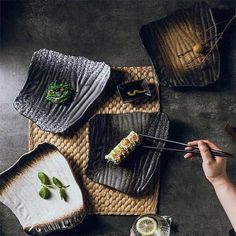 a person holding chopsticks over some food on a table with plates and bowls