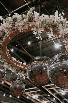 several disco balls hanging from the ceiling with flowers and greenery on them in front of a circular mirror