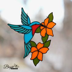 a stained glass hummingbird hanging on a branch with orange and blue flowers in the foreground