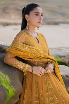 a woman in an orange dress standing next to a rock and looking off into the distance