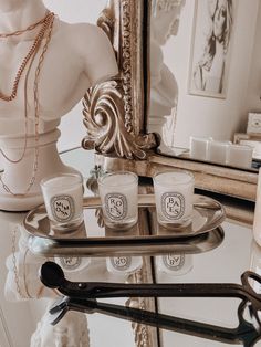 three candles on a tray in front of a mirror with a mannequin behind it