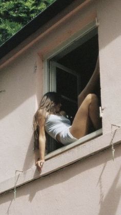 a woman leaning out the window of a pink building with her leg in the air