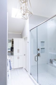 a white bathroom with a chandelier hanging from the ceiling and a walk in shower