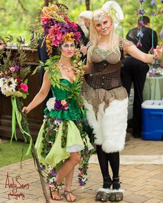 two women dressed in costumes standing next to each other with flowers on their heads and hands