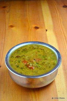 a metal bowl filled with green soup on top of a wooden table