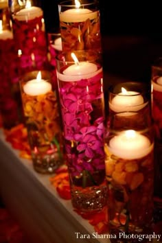 candles are lined up on a table with flowers and petals in vases next to each other