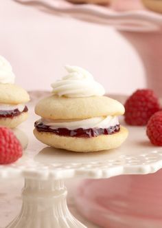 three raspberry shortcakes on a cake stand with fresh raspberries