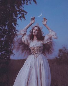 a woman in a white dress is holding her hands up to the sky while standing in a field