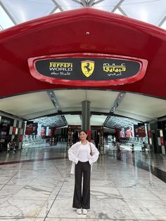 a woman is standing in front of a ferrari world sign at the entrance to an airport