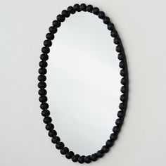 a black beaded necklace hangs on the wall in front of a round shaped mirror