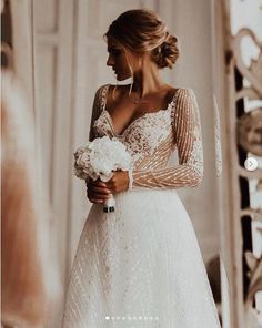 a woman in a white wedding dress holding a bouquet and looking at her reflection in the mirror