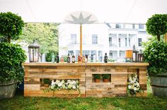 an outdoor bar made out of pallets with flowers and bottles on top, surrounded by potted plants