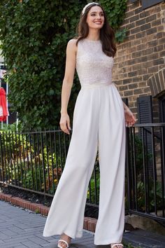 a woman standing on the sidewalk wearing white pants and a top with sequins