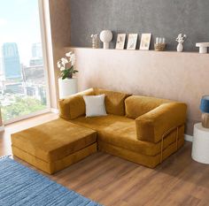 a living room with a large yellow sectional couch and blue rug on the wooden floor