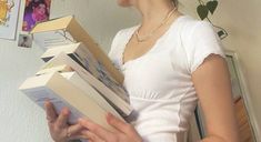 a woman is holding several books in her hands and looking at the wall behind her