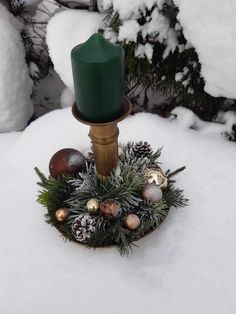 a green candle sitting on top of a snow covered ground next to pine cones and ornaments