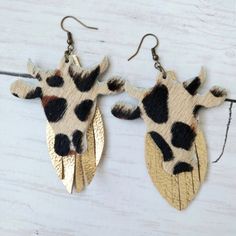 a pair of giraffe shaped earrings hanging from hooks on a white wooden surface