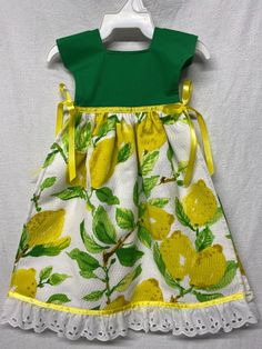 a white dress with yellow flowers and green trim on the front, sitting on a hanger