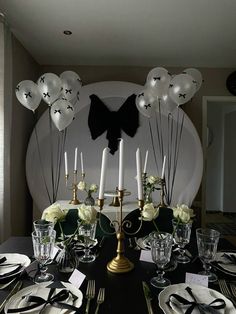 a black table topped with plates and silverware next to a wall decorated with balloons