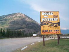 a large yellow sign sitting on the side of a road in front of a mountain