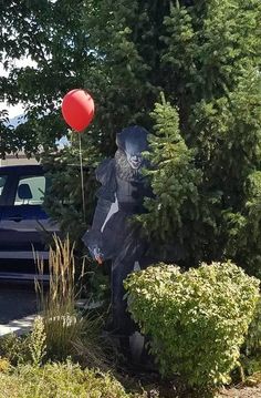 a statue of a bear holding a red balloon in front of some bushes and trees