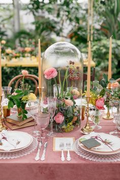 the table is set with pink flowers and greenery in glass dome vases on top