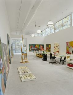 an artist's studio with paintings and easels on the wall, in front of windows