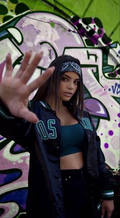 a woman standing in front of a graffiti wall with her hand up to the camera