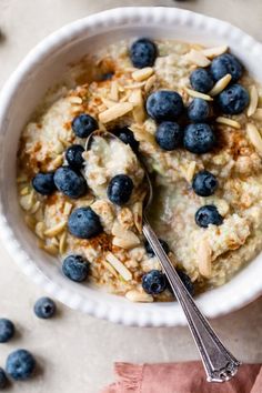 a bowl of oatmeal with blueberries and almonds next to a spoon