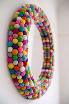 a multicolored wreath hanging on the side of a white wall next to a mirror