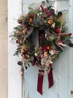 a wreath hanging on the side of a door decorated with flowers and foliage, next to a red ribbon