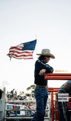 a man wearing a cowboy hat standing next to an american flag in front of a fence