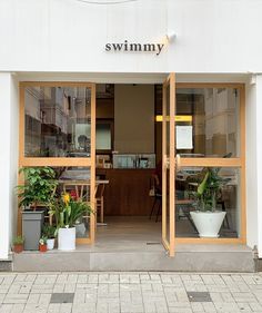 a store front with potted plants in the window and an open door that says swimmy