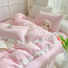 a bed with pink comforters and pillows on top of it next to a vase filled with flowers