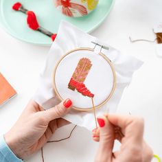 a woman is holding a cross - stitch pattern in front of her hand while she holds the needle