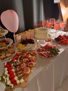 an assortment of food on a table with wine glasses and balloons in the background at a party