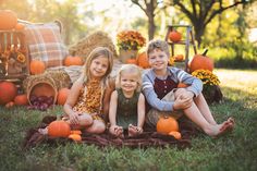 three children sitting on a blanket in front of pumpkins