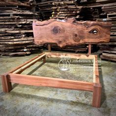 a bed frame made out of wood sitting in front of stacks of wooden planks